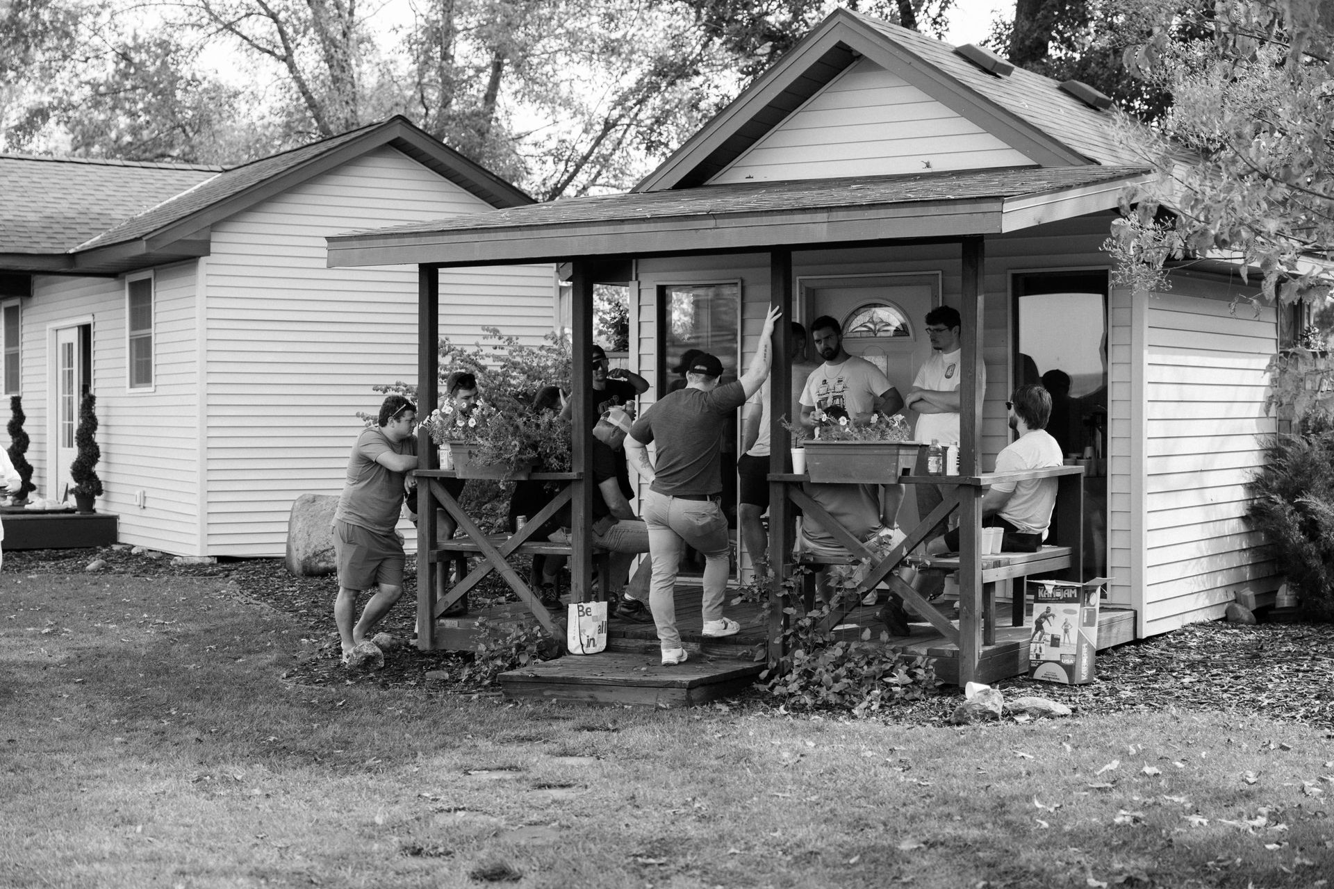 Group of people on porch of white building. Some stand inside doorway.