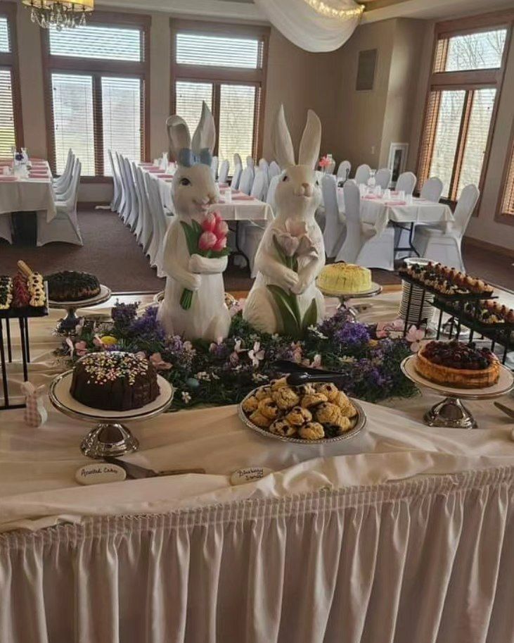 Easter dessert buffet with bunny decorations, cakes, and pastries on a long, white-skirted table.