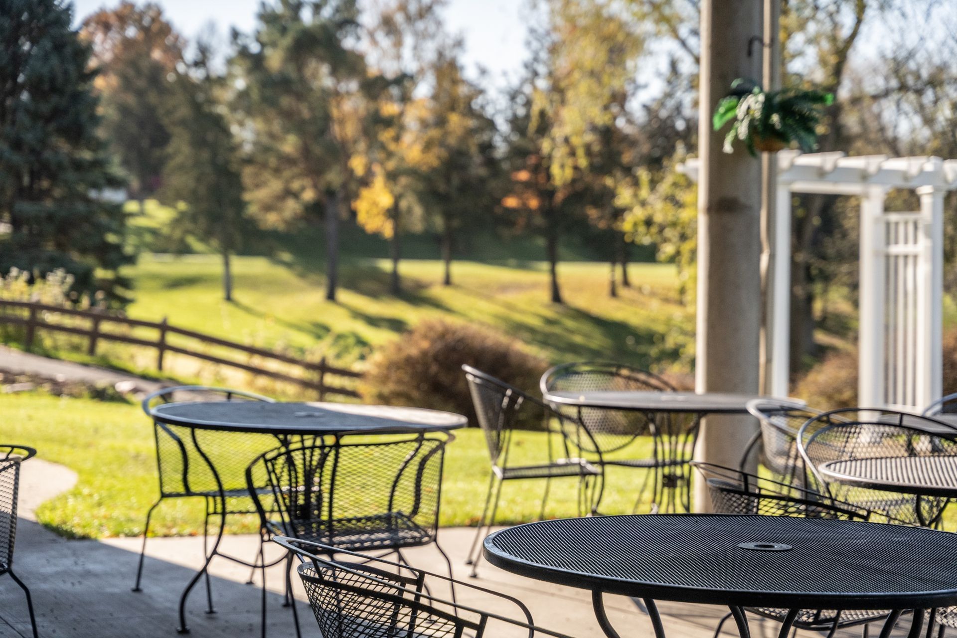 Outdoor patio with black metal tables and chairs, overlooking a grassy hill with trees.