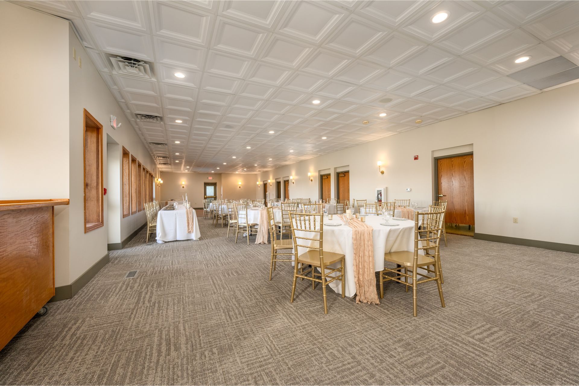 Empty banquet hall with round tables set for a formal event. Tables draped in white linens with peach accents.