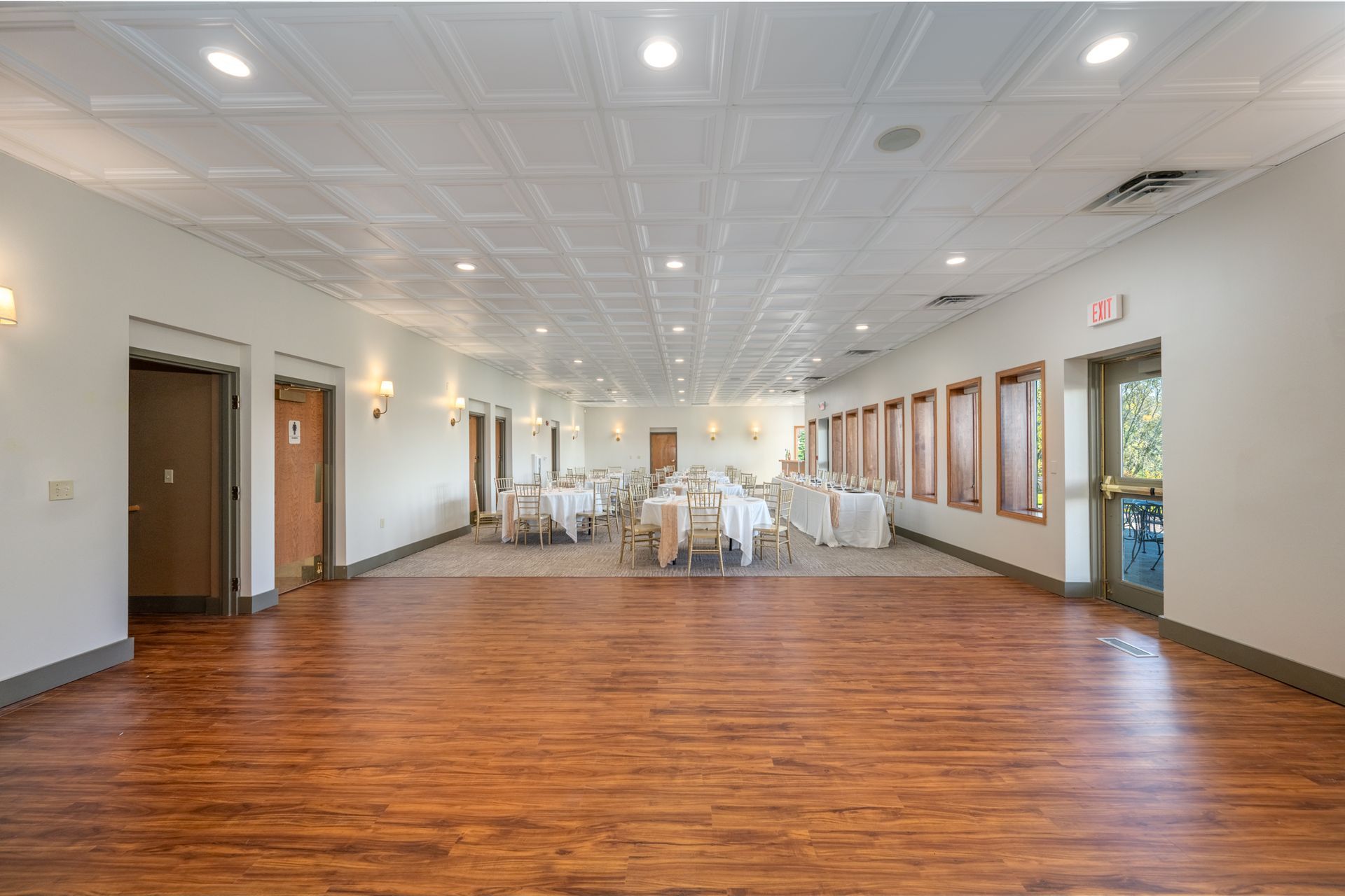 Empty event space with wood floor, white walls and ceiling, tables set up.