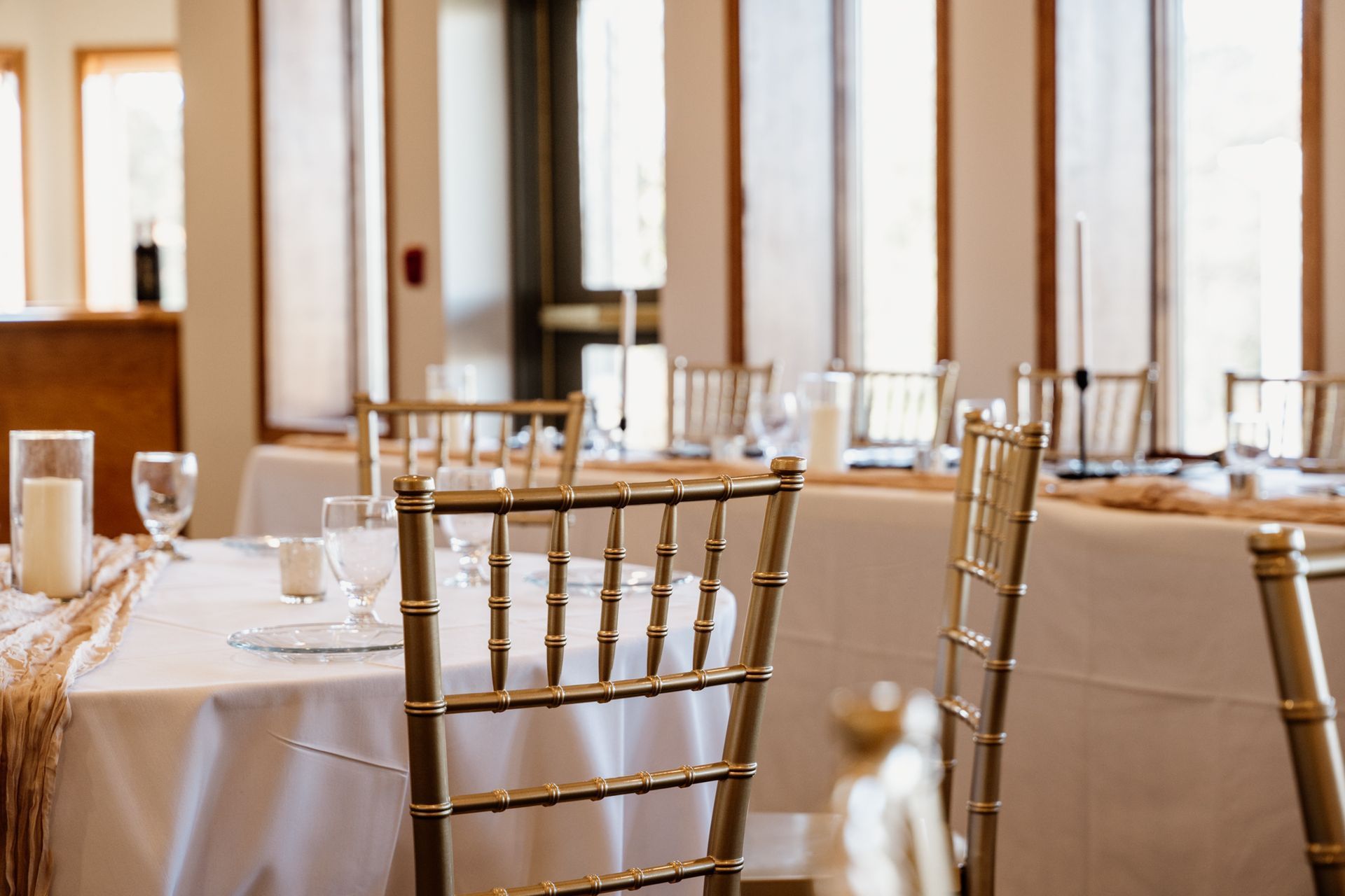 Elegant table setting with gold chairs and white tablecloth in a bright room.
