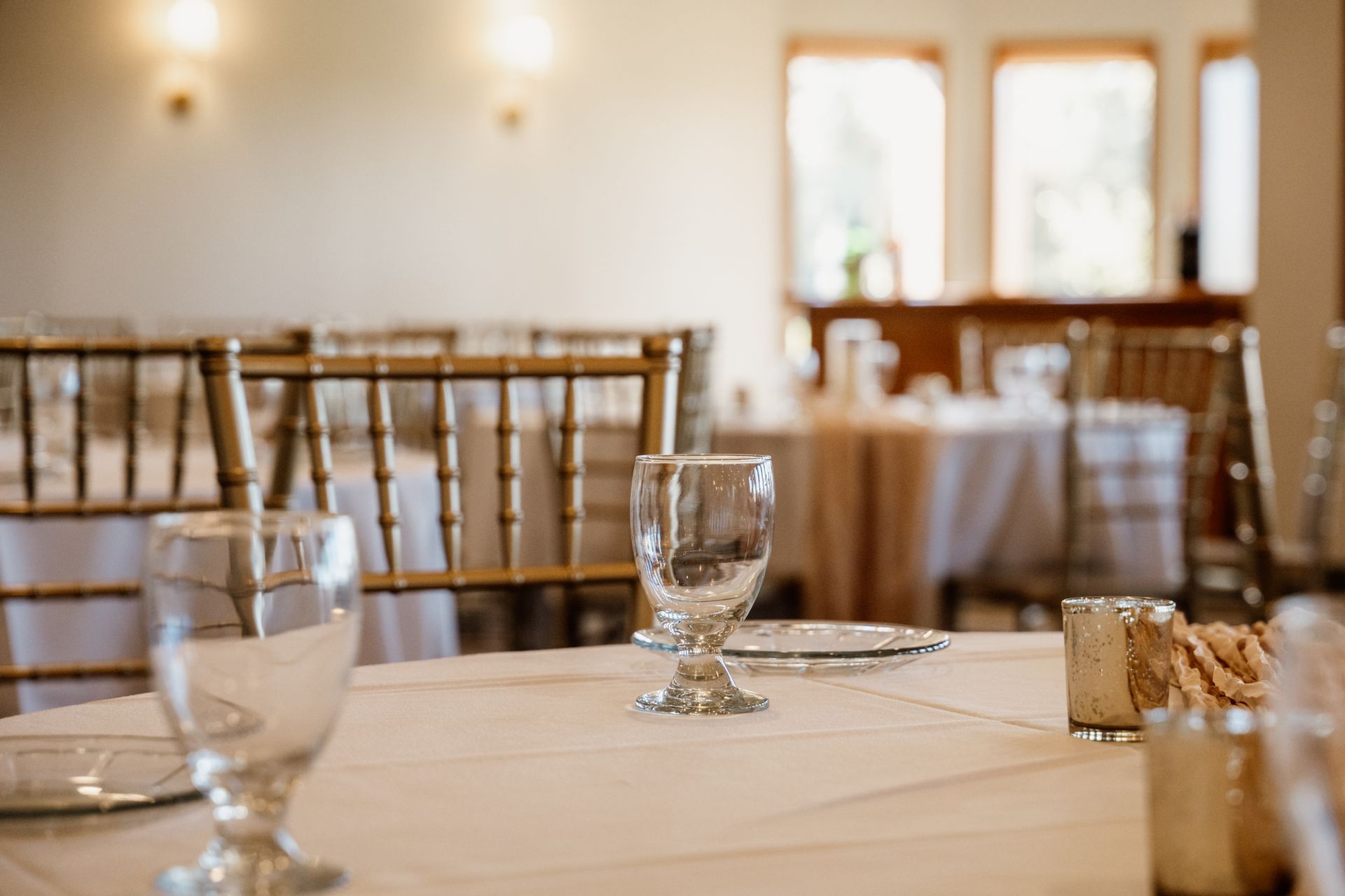 Elegant table setting in a banquet hall, with gold chairs and white tablecloths.