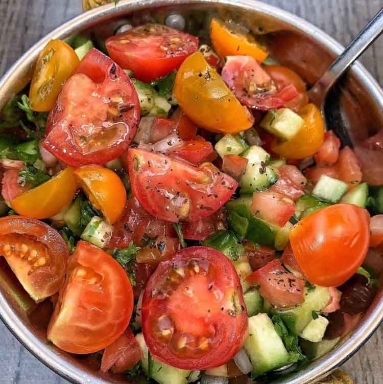 A bowl filled with tomatoes , cucumbers , and other vegetables with a spoon in it.