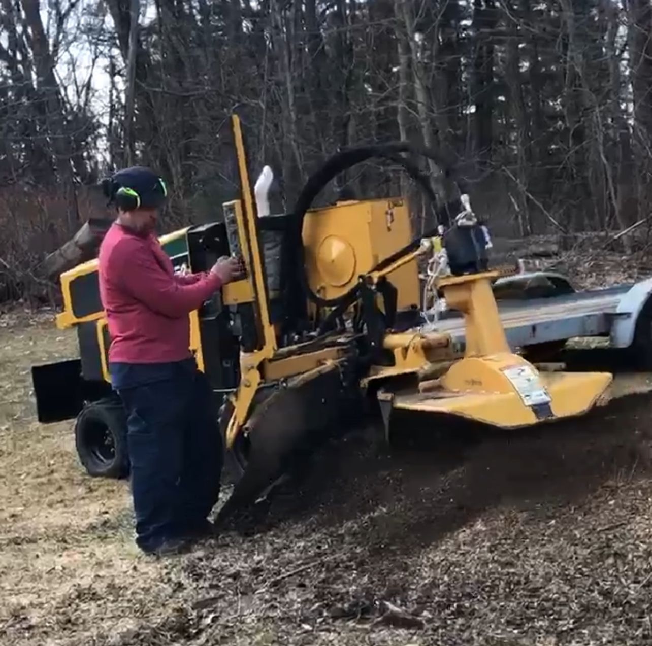Person operating a yellow stump grinder outdoors, chipping wood.