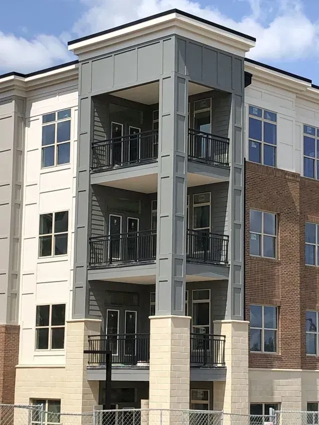 Multi-story building with balconies, brick, and gray siding under a bright sky.