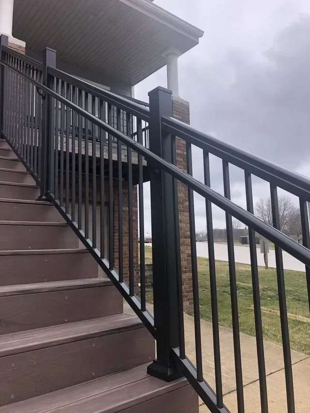 Black metal railing on brown stairs leading up to a building, overcast sky.