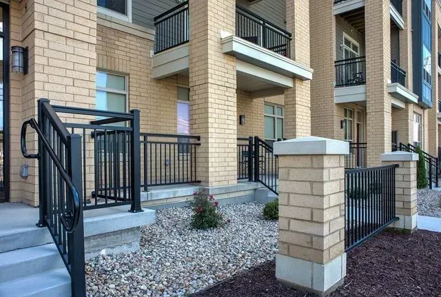 Exterior of a building with brick pillars and black metal railings on a stone pathway and entrance steps.