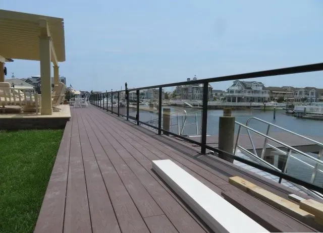 Wooden dock with black railing, glass panels, overlooking a canal, blue sky.