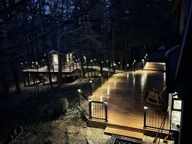 Lit wooden deck at night with surrounding trees and pathway lights.