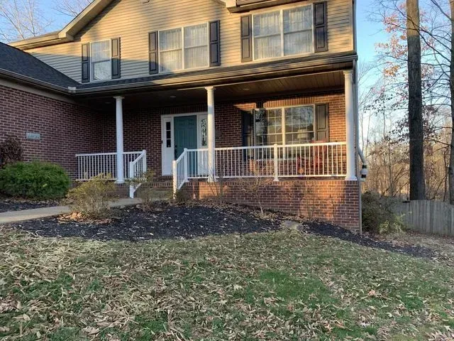 Two-story brick house with a front porch, white railings, and a blue front door; overcast day.