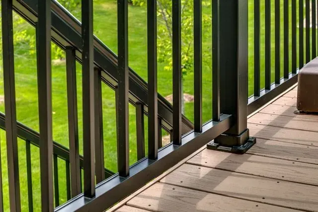 Black railing on wooden deck with green grass in the background.