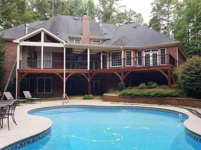 Backyard with pool and two-story brick house with deck and screened porch.