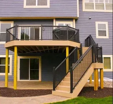 Two-story deck with stairs, black railing, tan deck, and yellow supports against a blue house.