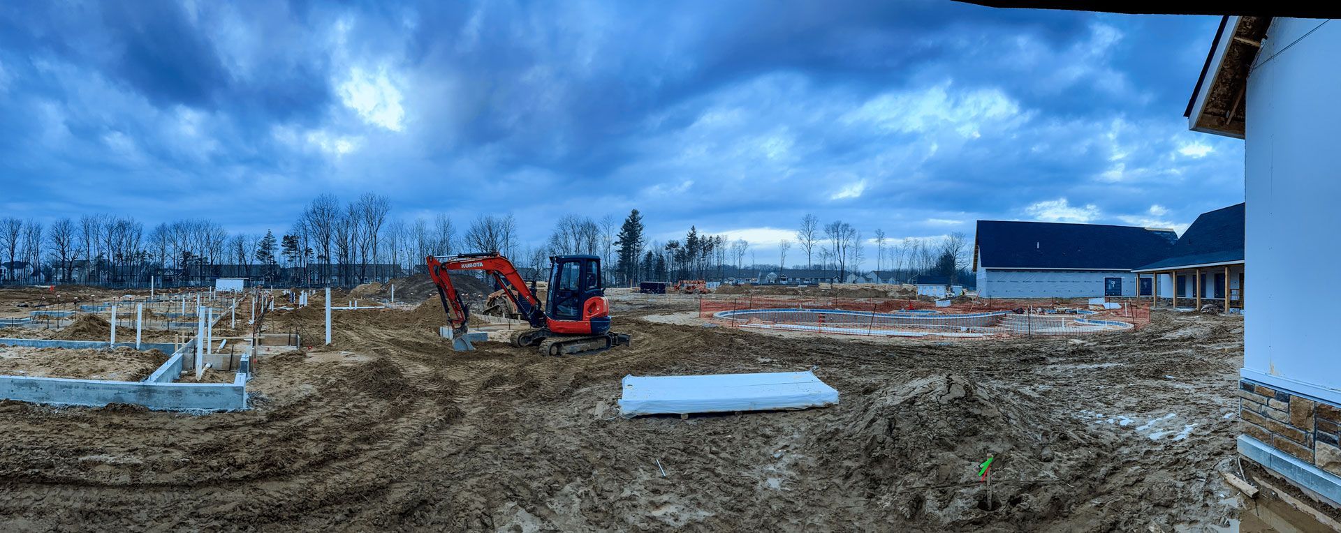 A panoramic view of a construction site with a house in the background.