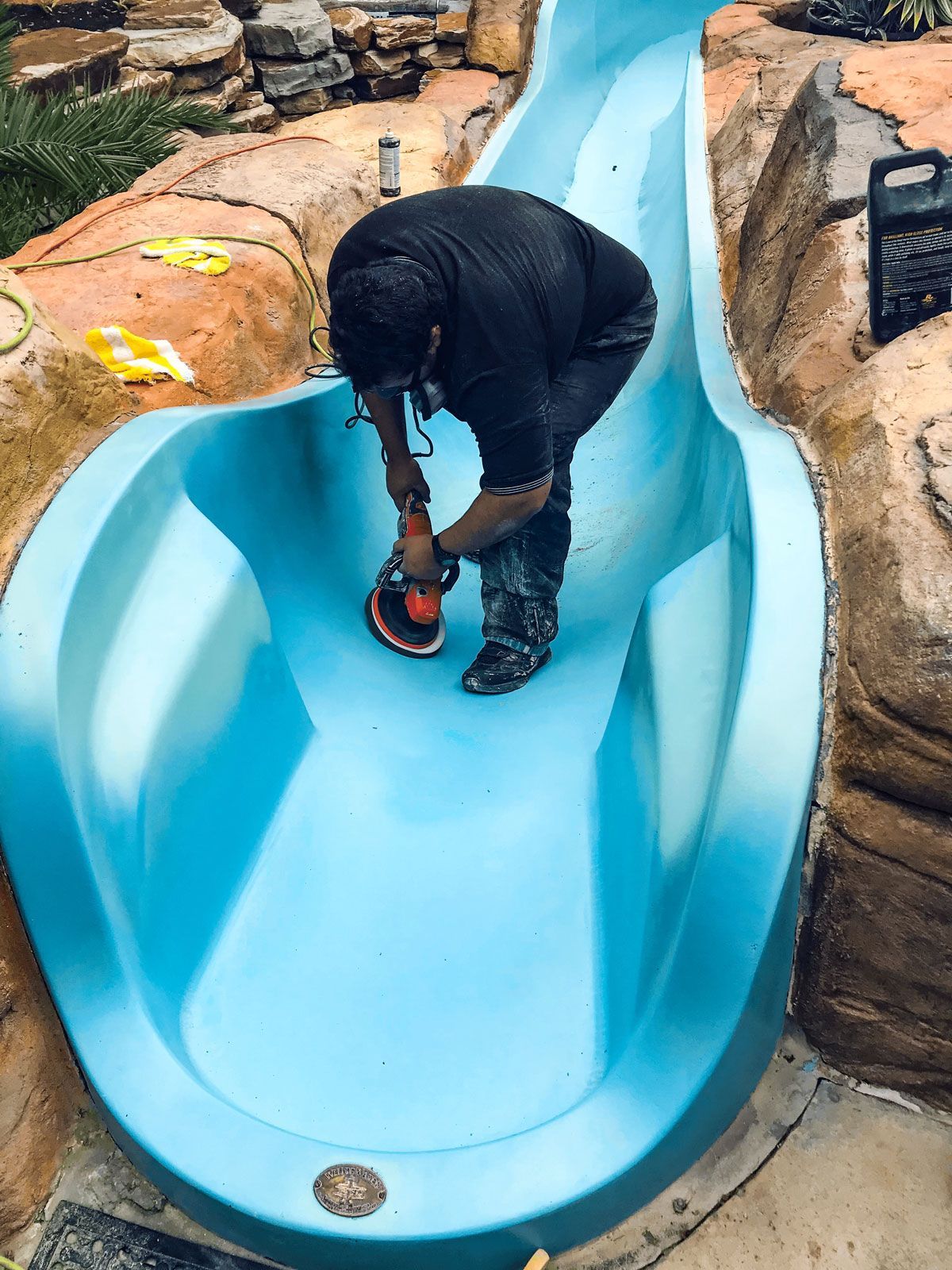 A man is polishing the bottom of a blue water slide.