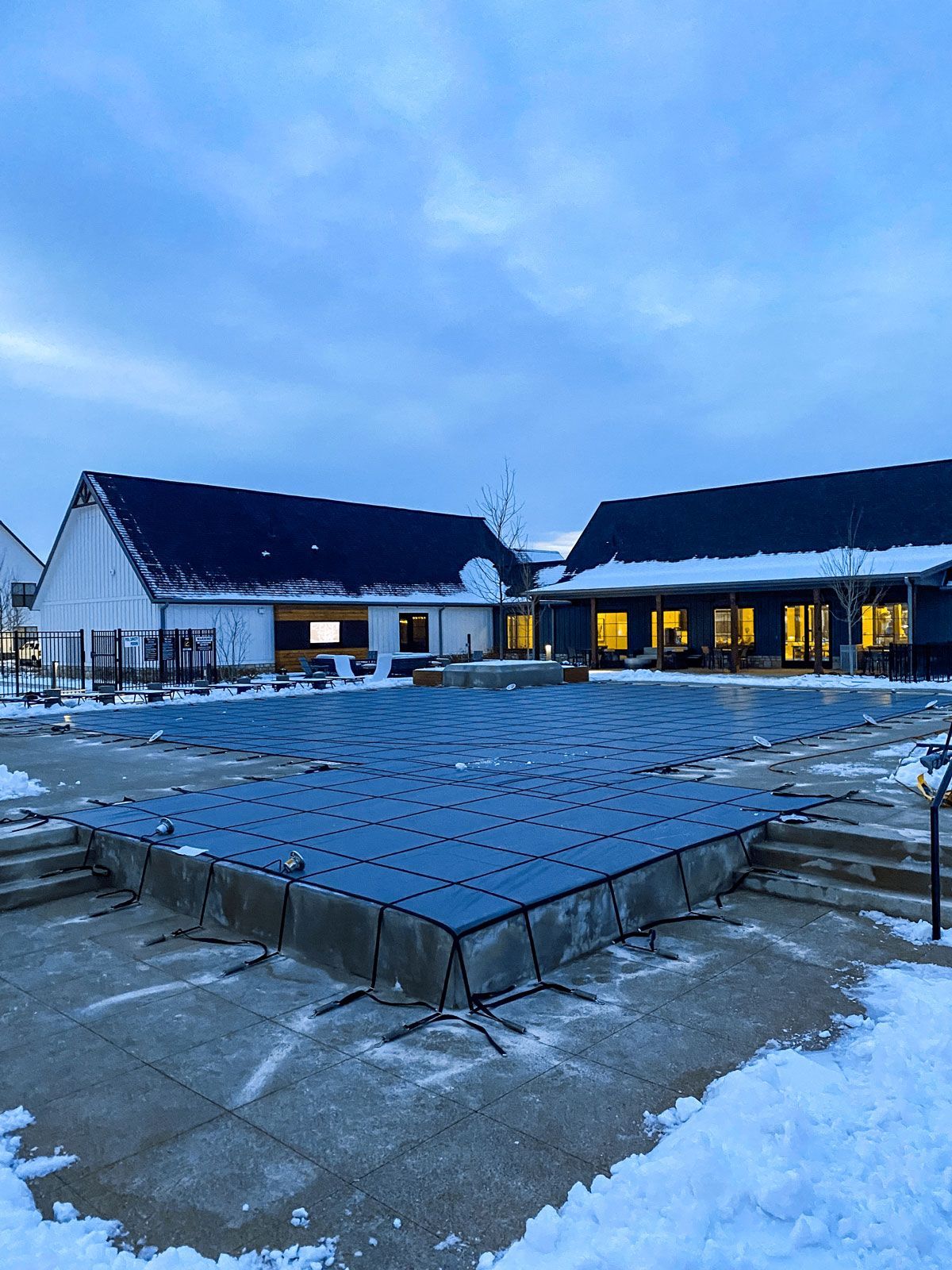 A large swimming pool is covered with a blue cover in the snow.