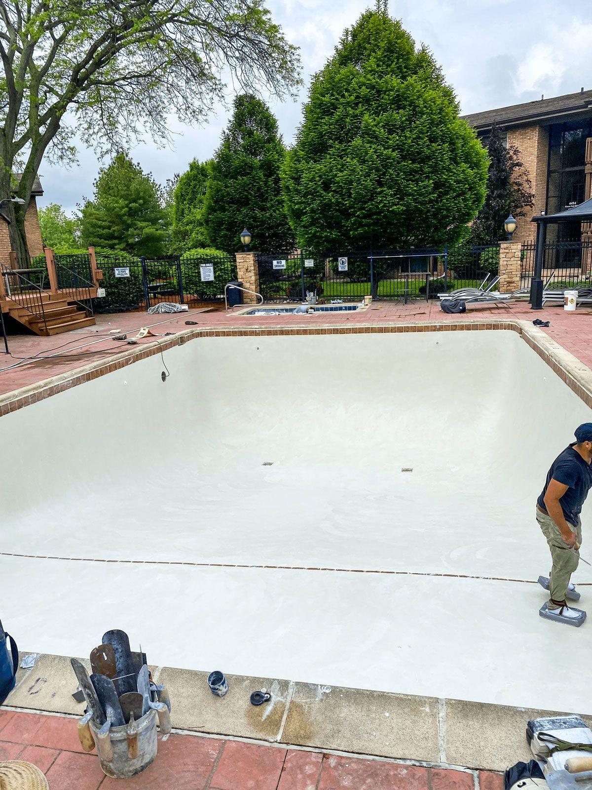 A man is painting a swimming pool with white paint.