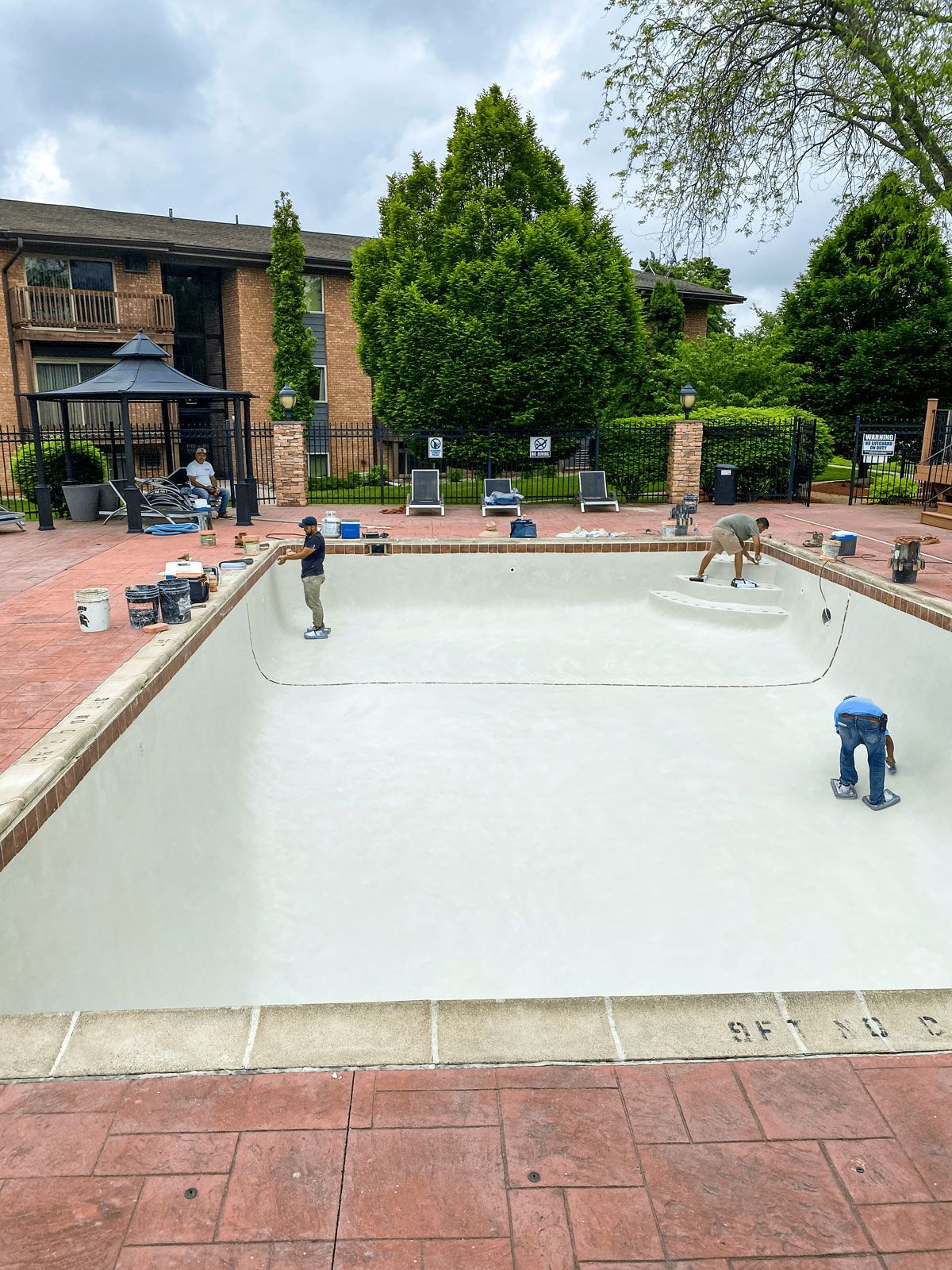Two men are working on a swimming pool in front of a building.