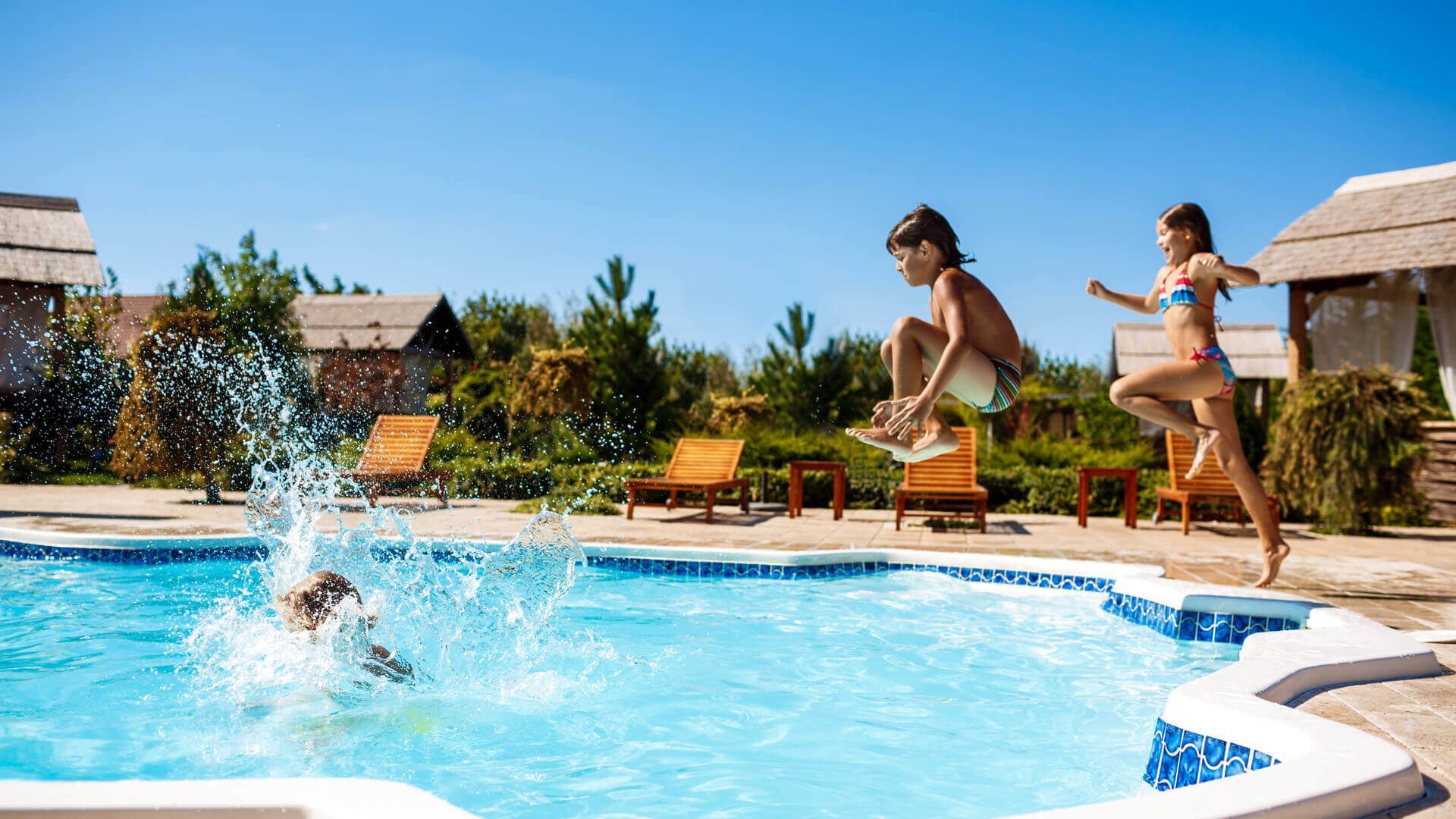 A boy and a girl are jumping into a swimming pool.