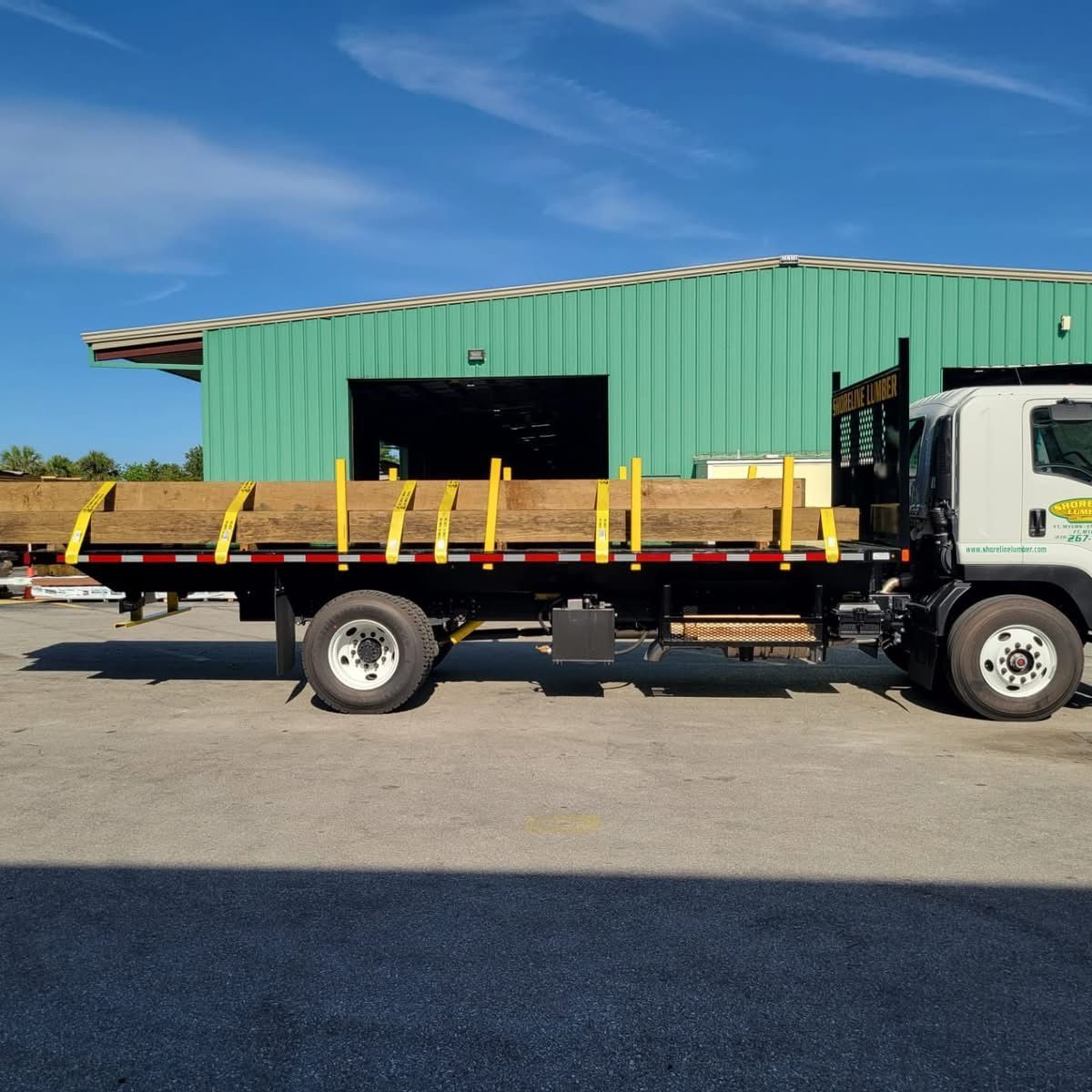 A flatbed truck is parked in front of a green building
