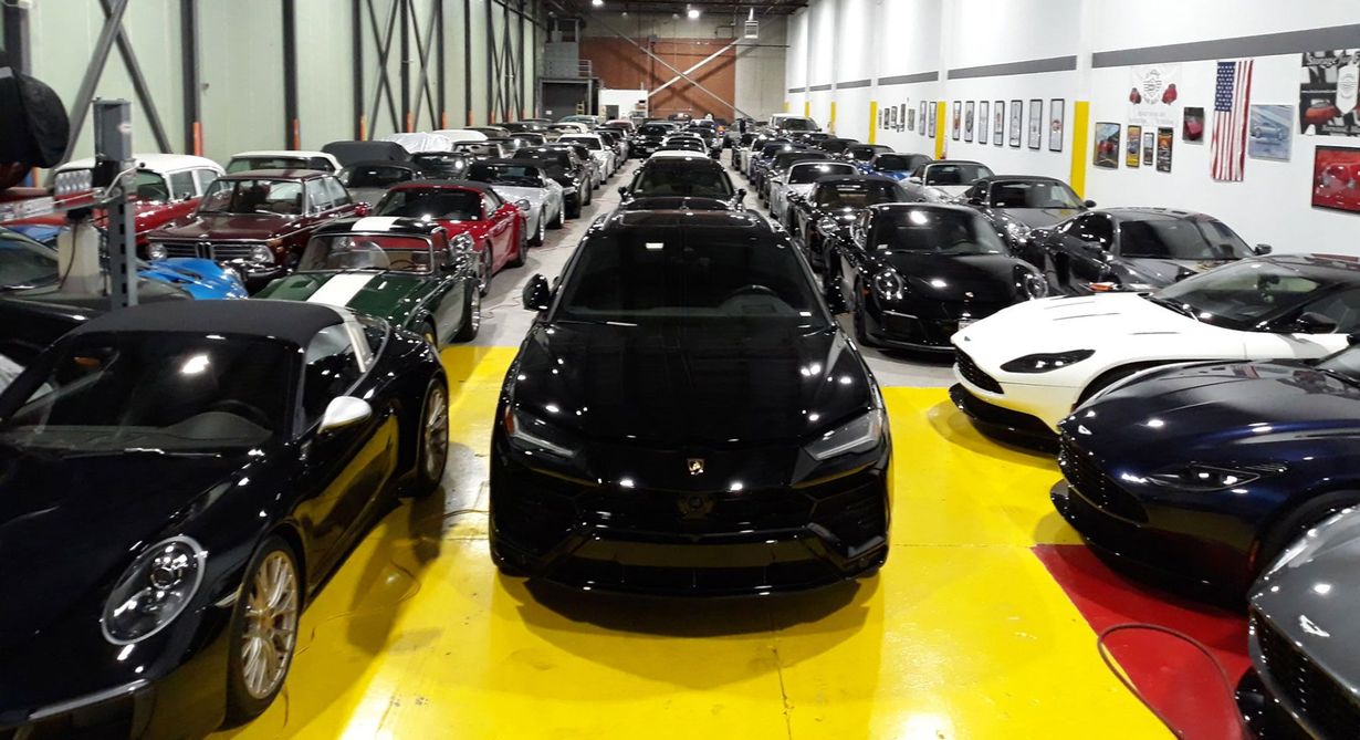 Rows of luxury sports cars in a showroom, centered on a black car on a yellow floor