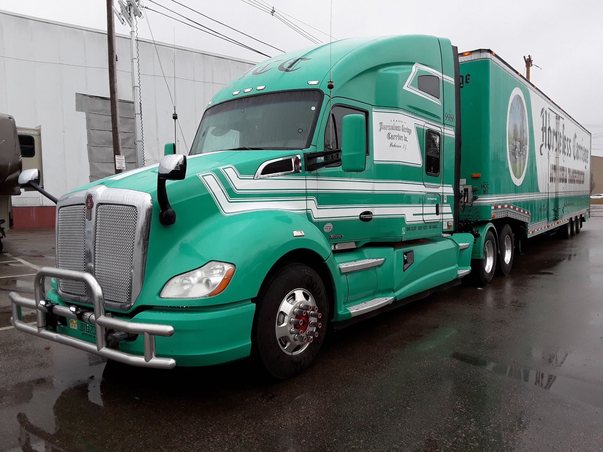 Green semi-truck with trailer parked on a wet road under overcast sky