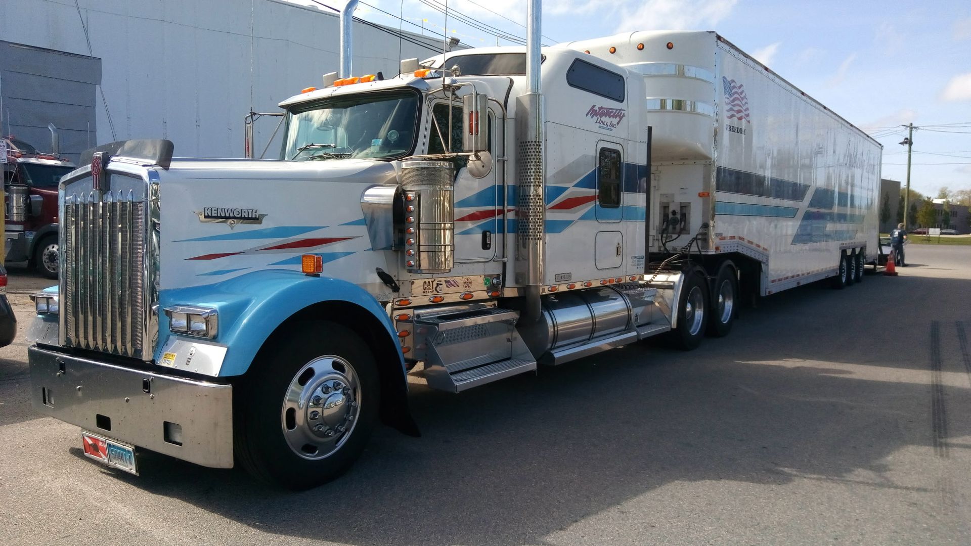 Silver semi truck with chrome details parked on pavement outside a building