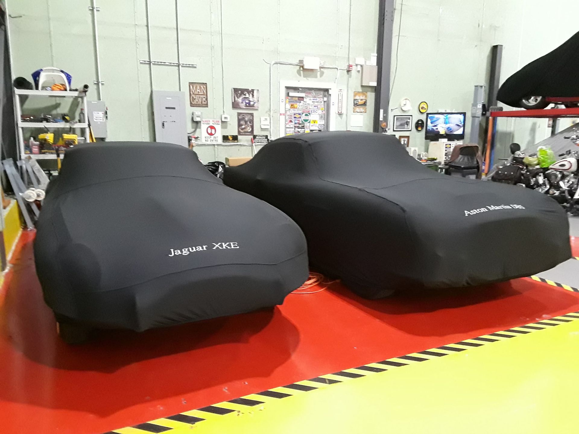 Two black car covers on a red showroom floor inside a garage or workshop.