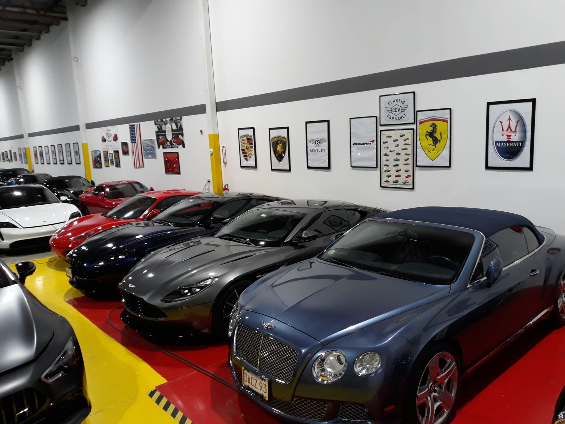 Sports cars lined up in a showroom, including a blue Bentley in front and a red Ferrari behind.
