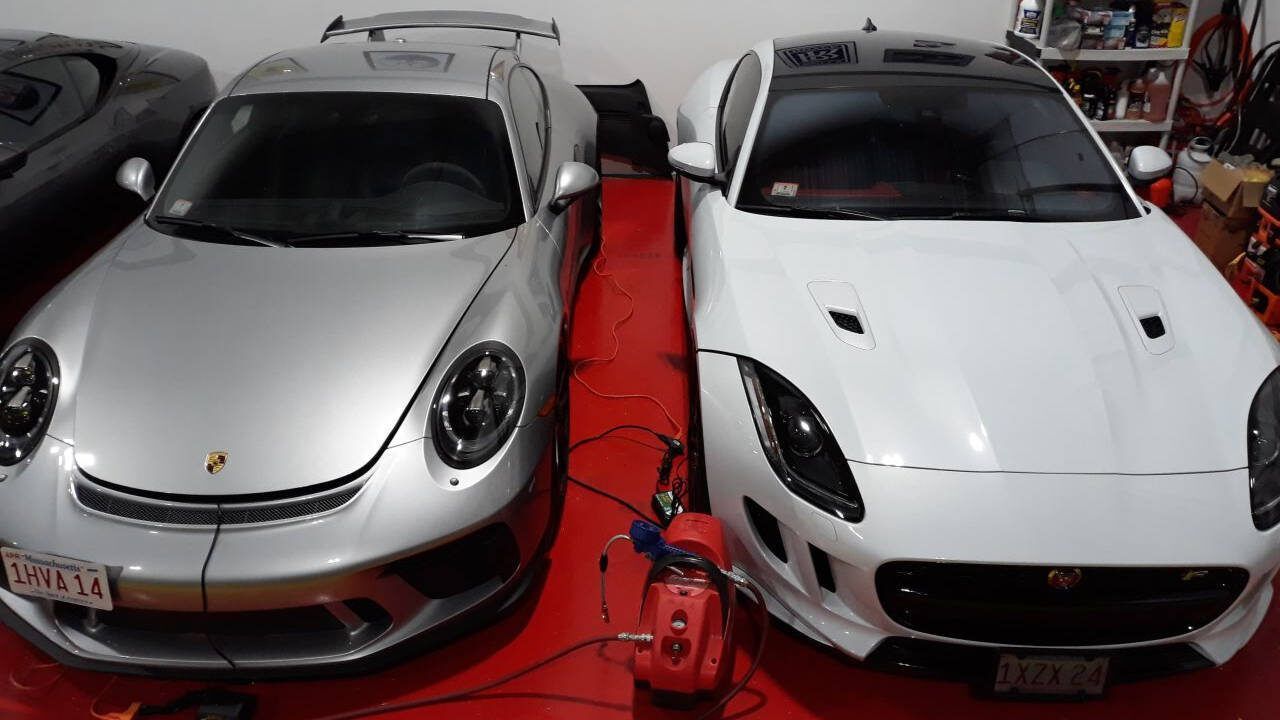 Two silver sports cars parked side by side in a garage with red floor mats