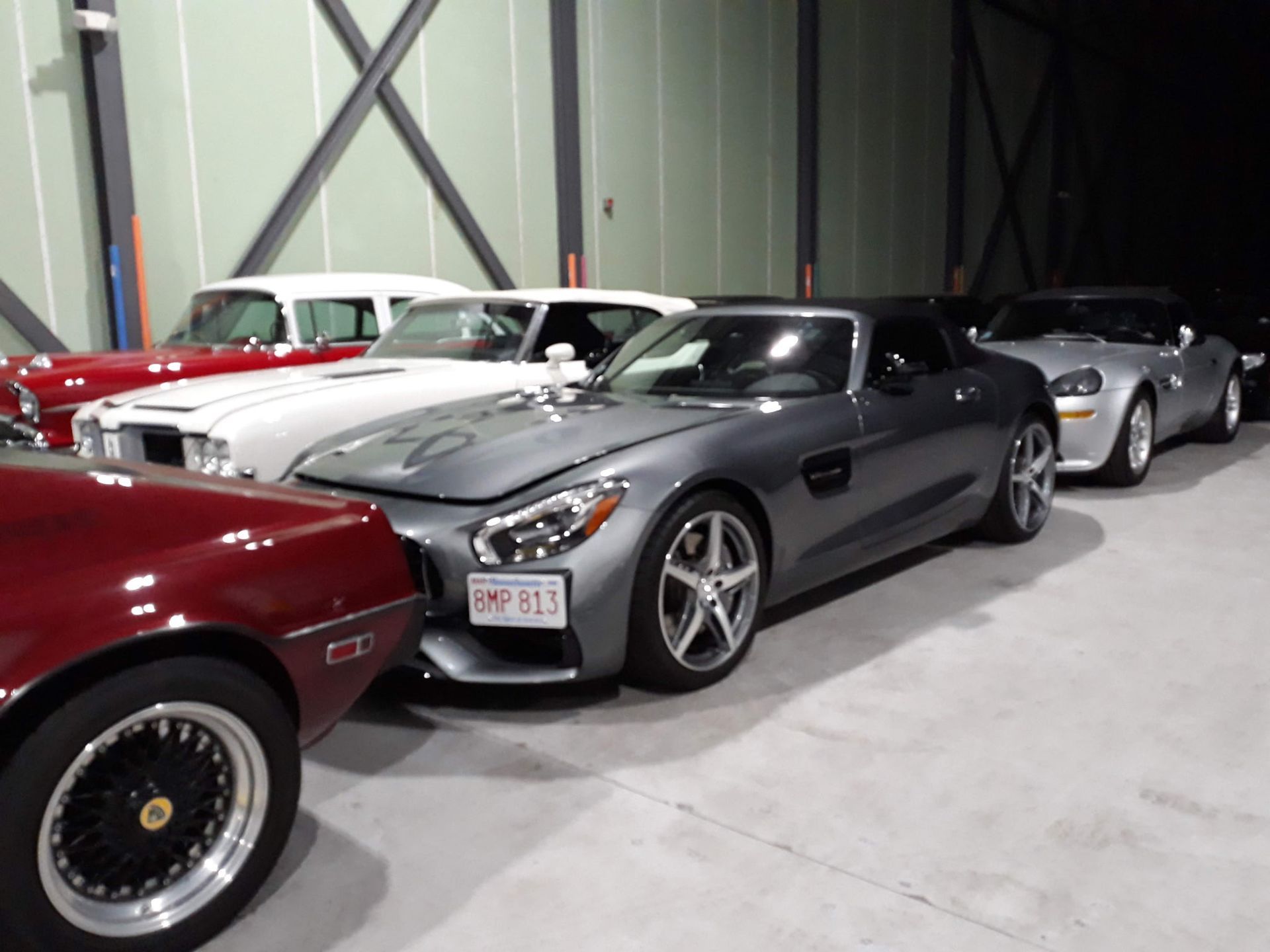 Classic sports cars parked indoors, led by a dark gray convertible with red and white cars behind it