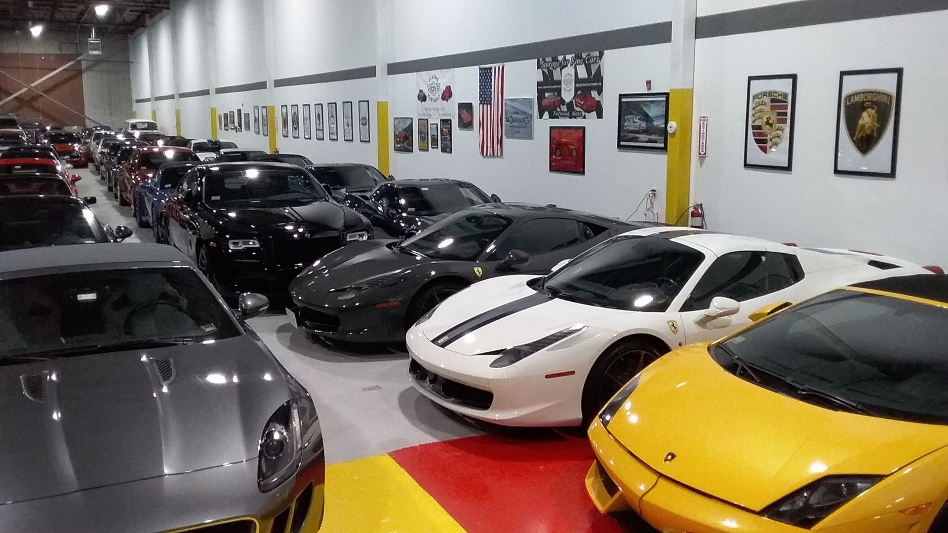Row of luxury sports cars in an indoor showroom, including silver, black, white, and yellow vehicles