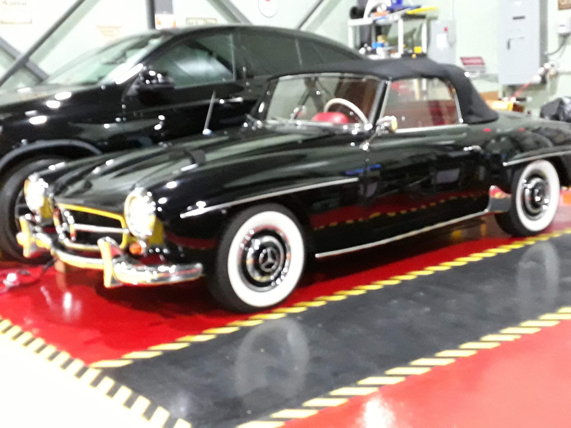 Black vintage convertible with whitewall tires displayed on a red platform in a garage showroom