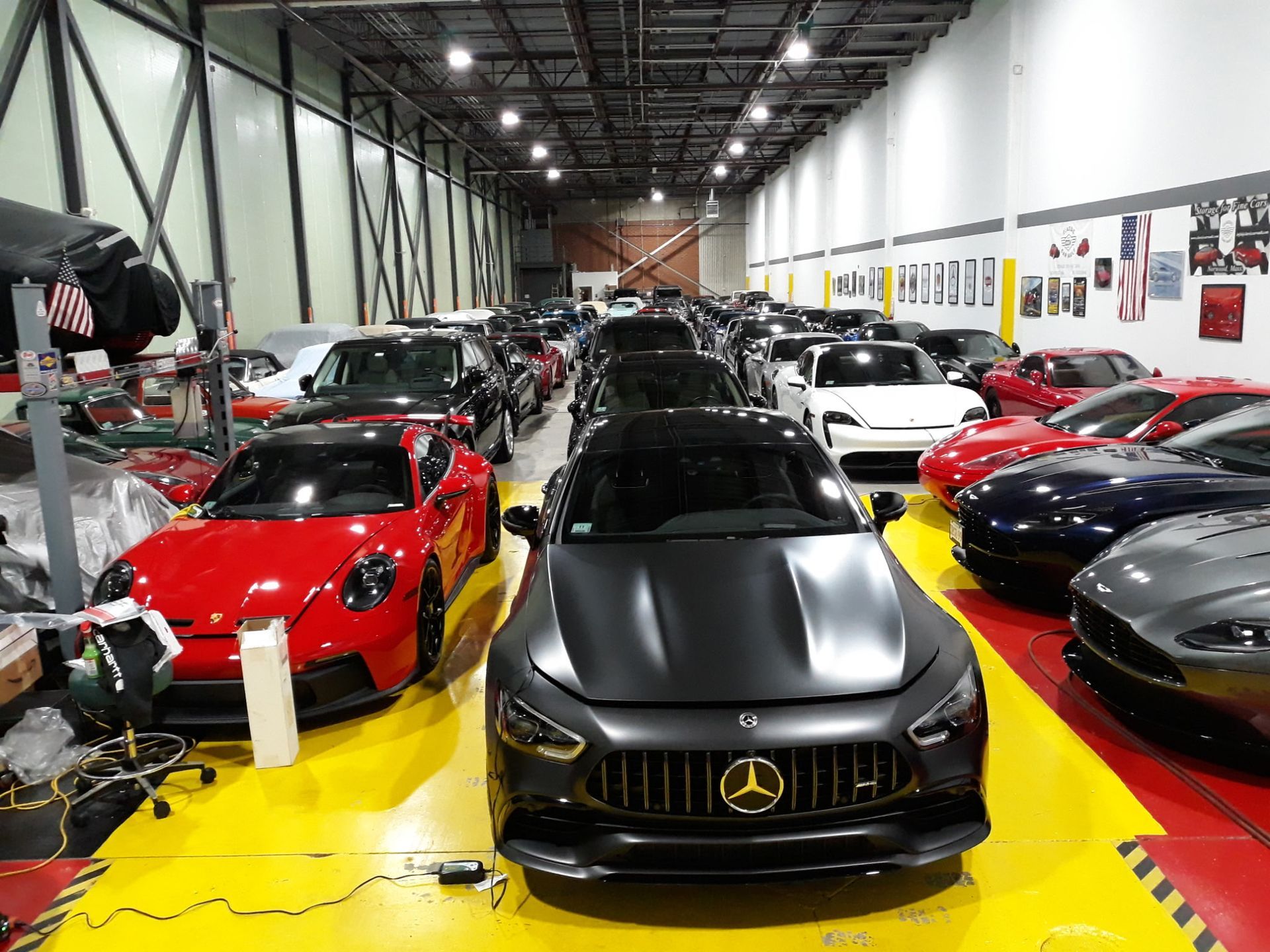 Sports cars displayed in a showroom, with a matte black Mercedes centered on a bright yellow floor.