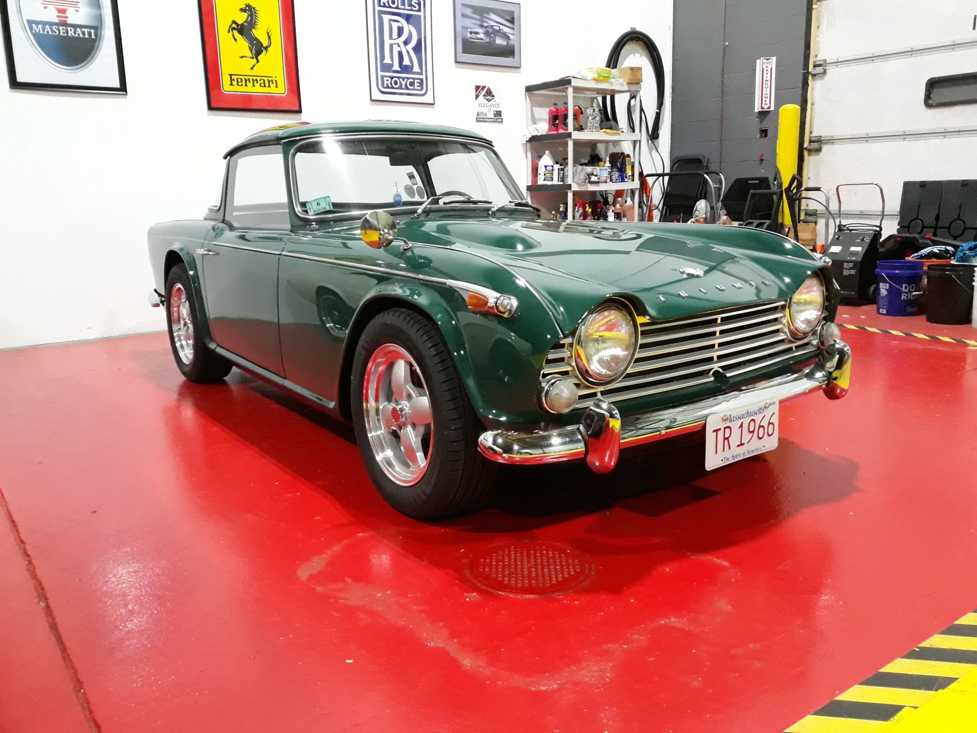 Green classic convertible in a garage with glossy red floor and car memorabilia on the wall