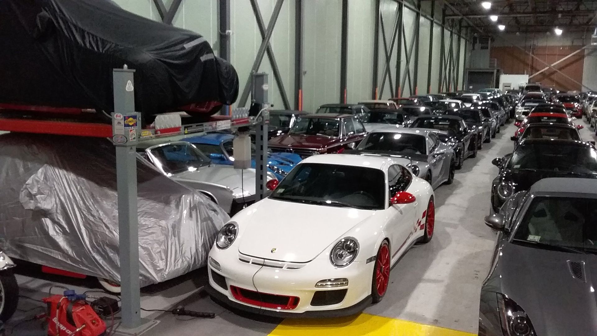 Rows of luxury sports cars stored in a warehouse, with a white Porsche centered in front.