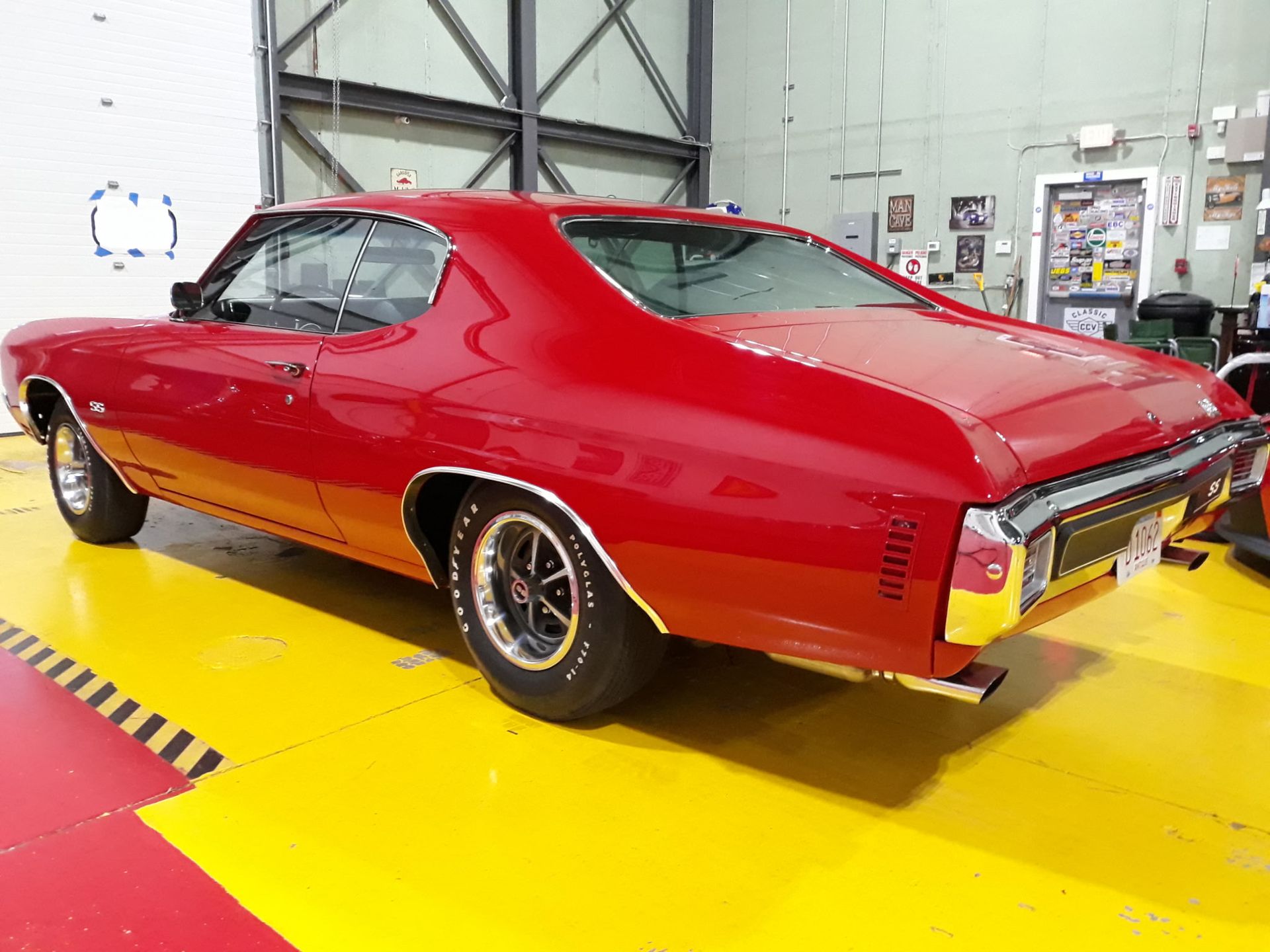 Red classic muscle car in a workshop, viewed from the rear side on a yellow floor.
