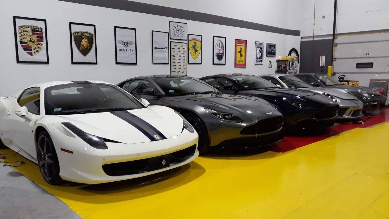Row of sports cars in a showroom, including a white car with black racing stripes in front