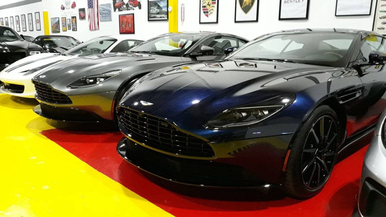 Luxury sports cars lined up in a showroom, with a black car in front on a red and yellow floor.