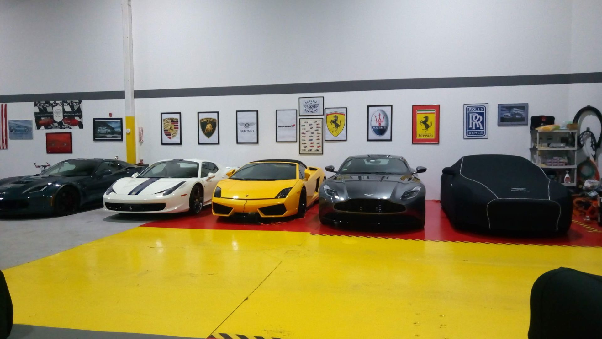 Luxury sports cars lined up in a showroom with bright yellow floor and framed wall art.