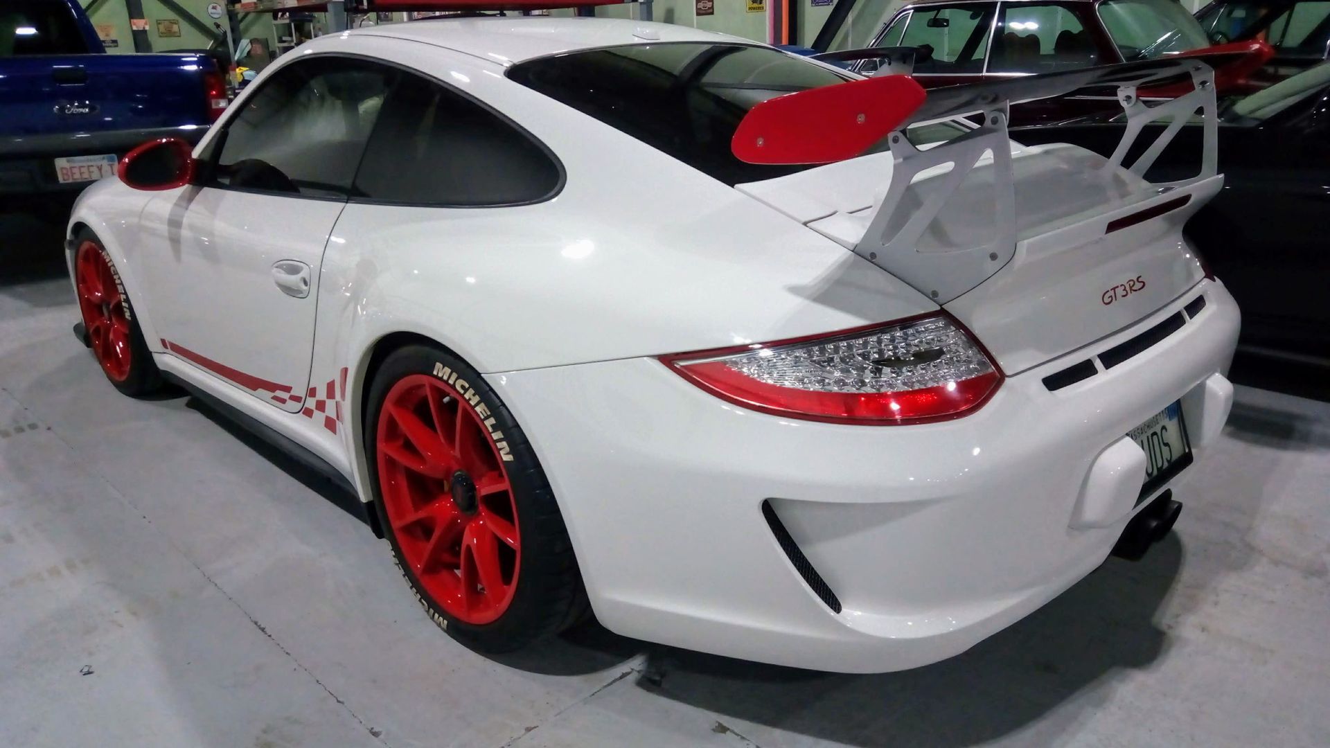 White sports car with red rims and a large rear wing displayed indoors at an auto show