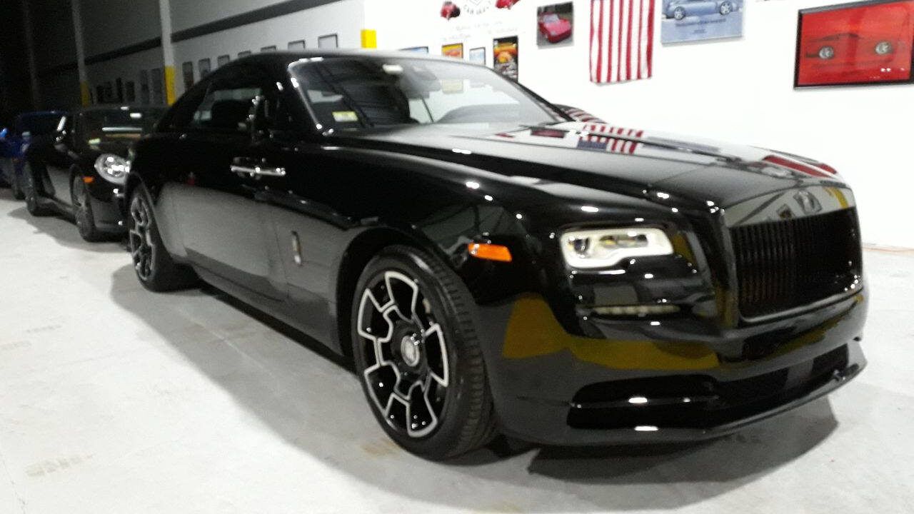 Black luxury Rolls-Royce parked indoors with red pinstripes and chrome wheels