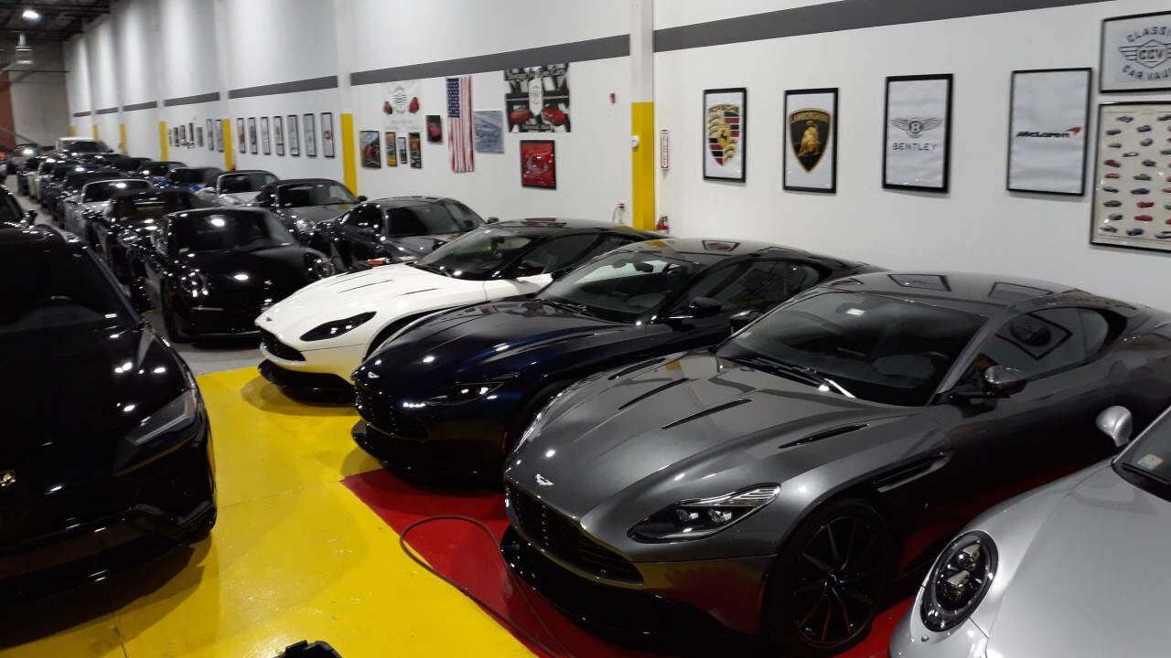 Rows of sports cars parked in a showroom with white walls and framed car posters.