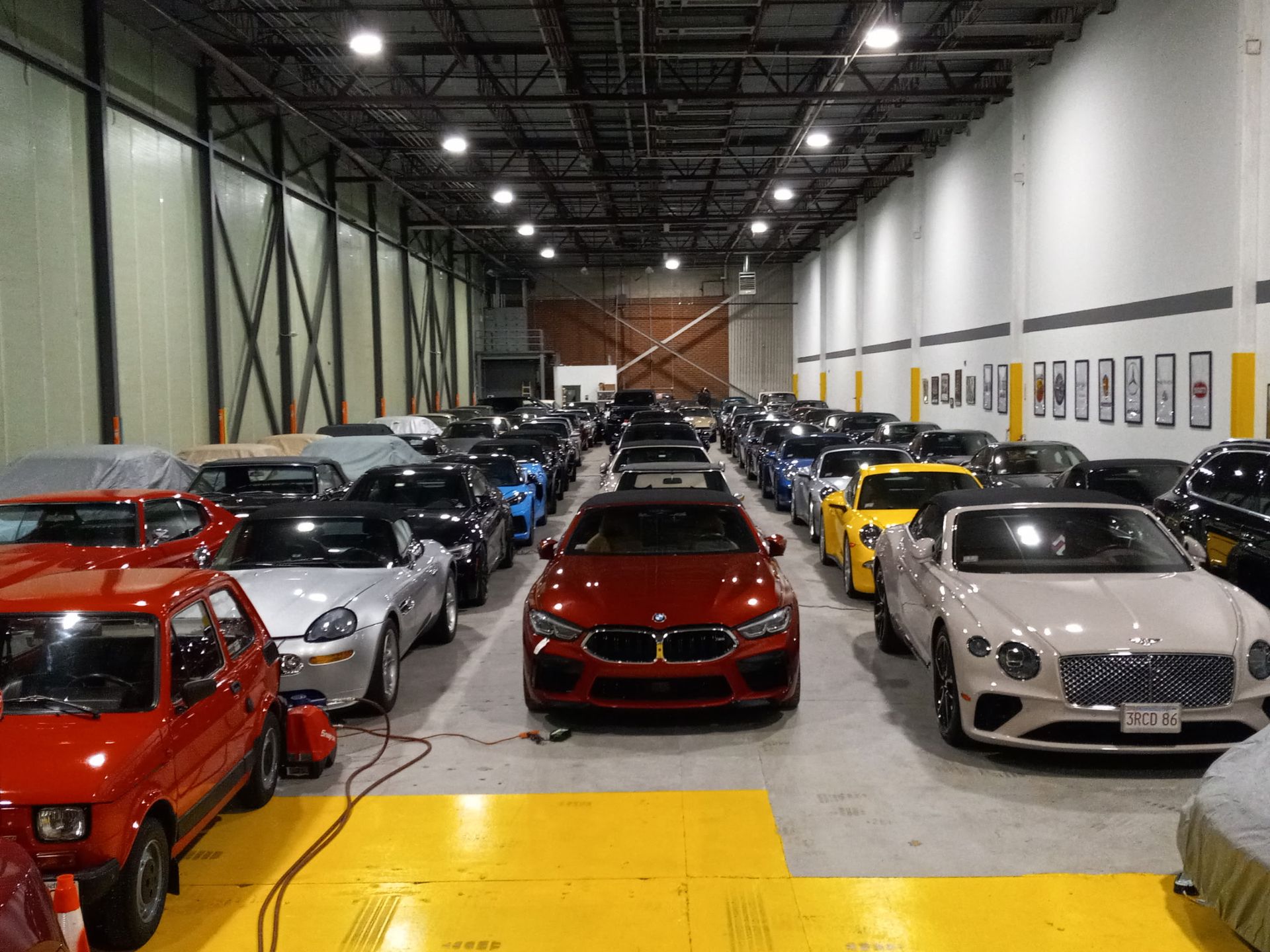 Rows of sports cars and luxury cars parked inside a large warehouse showroom with bright overhead lights