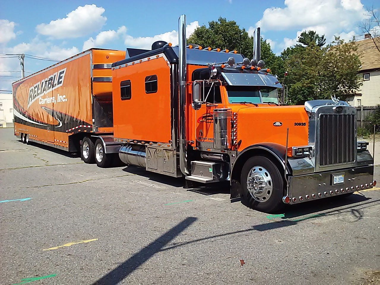 Orange Freightliner semi-truck with matching trailer parked on a street under a blue sky.