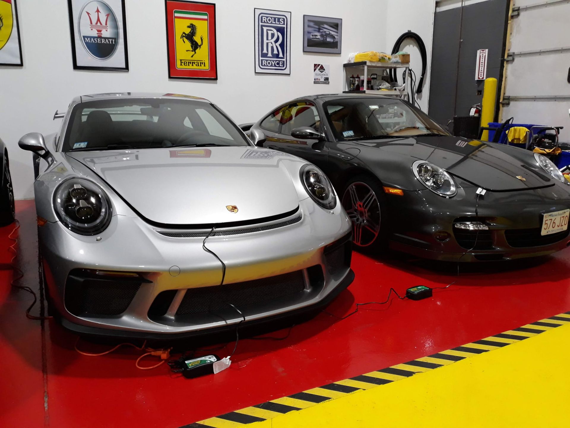Two Porsche sports cars, one silver and one black, displayed in a showroom with red floor and racing signs.