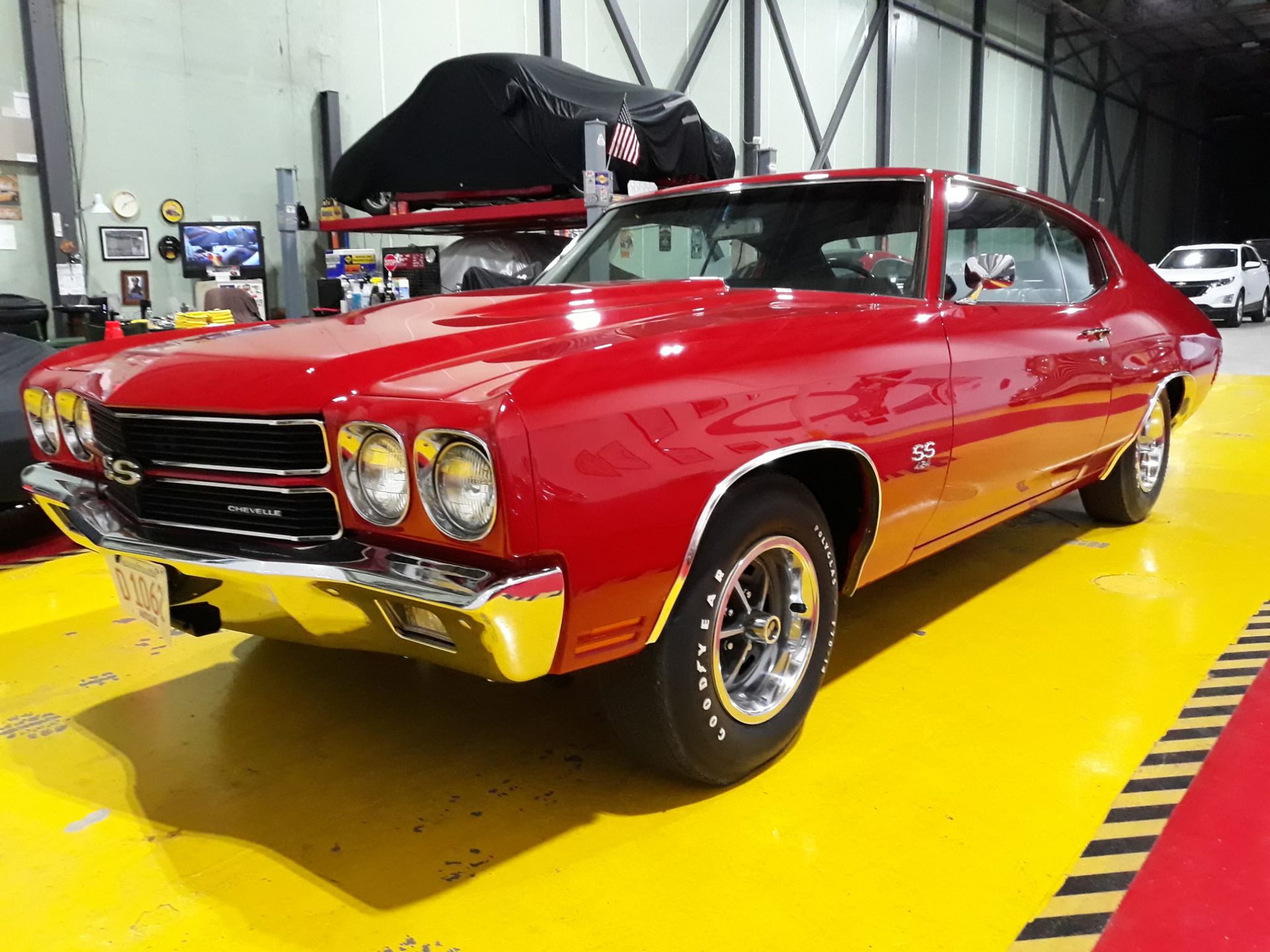 Red classic muscle car on display in a garage, with chrome details and black racing stripes