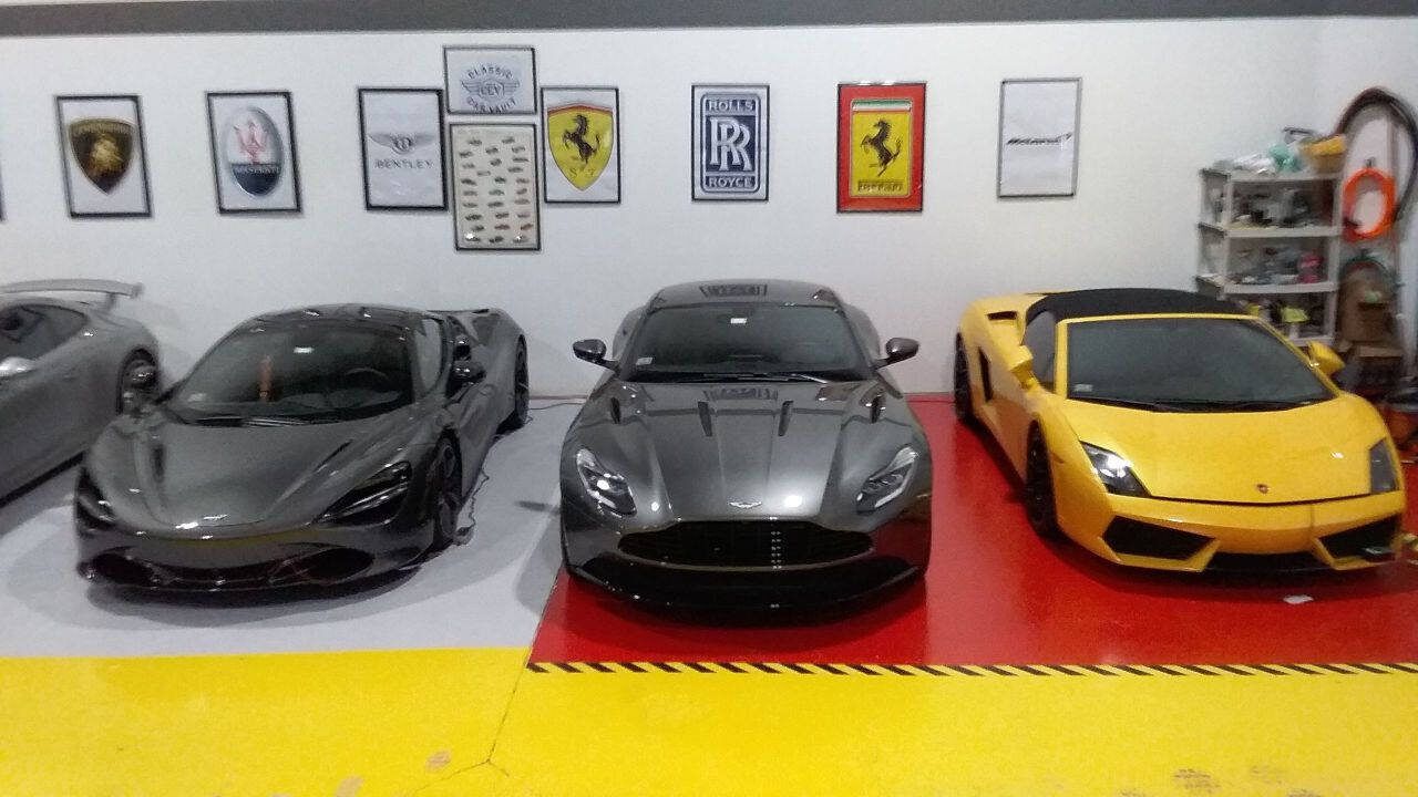 Three luxury sports cars—gray, black, and yellow—displayed indoors on a showroom floor.