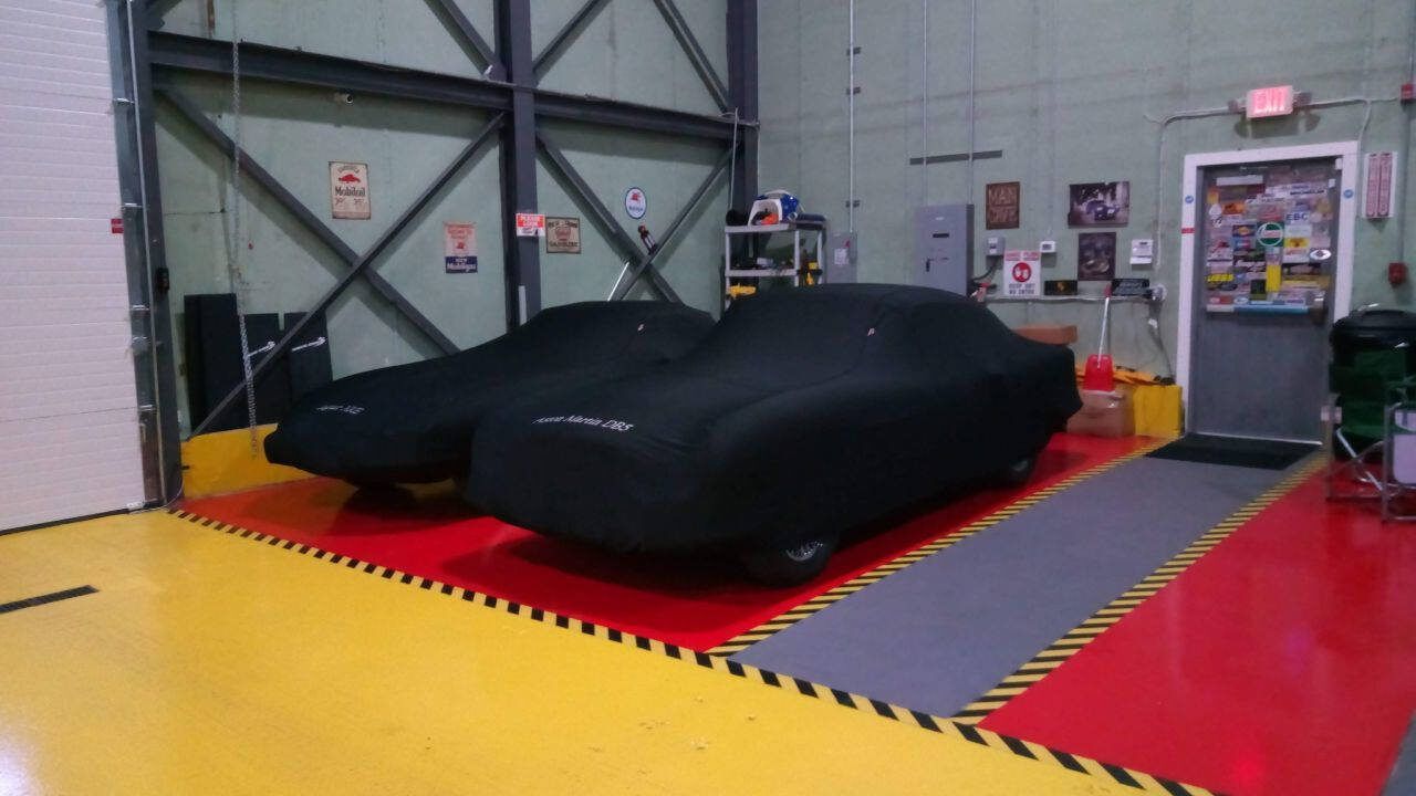 Black sports car under a cover in a garage with yellow and red floor markings